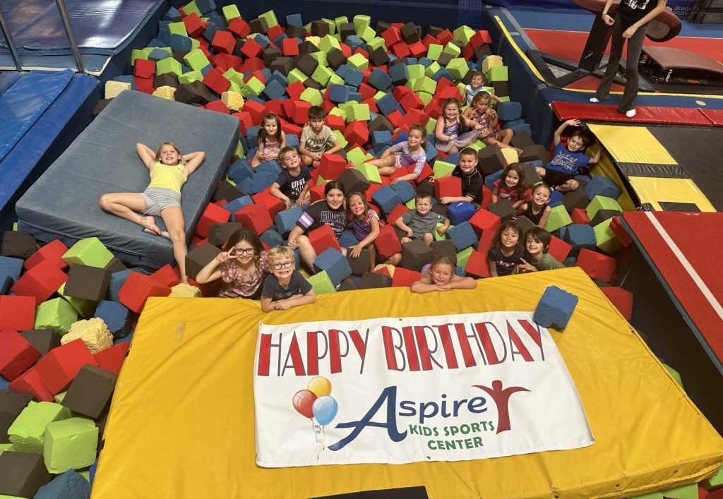 Kids in a colorful gymnastics pit with a yellow mat and a sign that says happy birthday